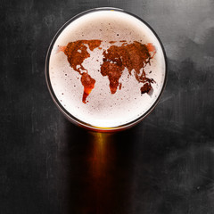 world map silhouette on foam in beer glass on black table. The continents shapes are altered ones...