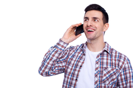 Nice to hear you! Cheerful young man talking on mobile phone and looking away with smile while standing against white isolated background