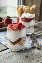 Sweet dessert in glass with biscuit, strawberry, mashed banana and whipped cream, selective focus