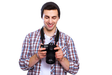 Great shot! Handsome young man holding digital camera and looking at it with smile while standing against white isolated background