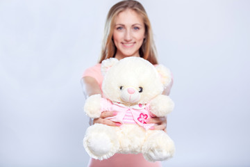 I have a gift for you! Attractive young women with teddy bear while standing over gray background