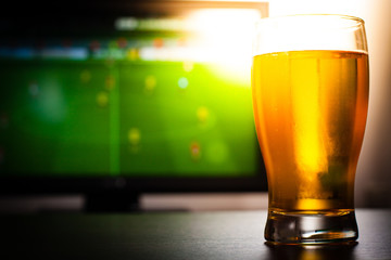 Pint of beer on the tabele in front of televisor show off football..