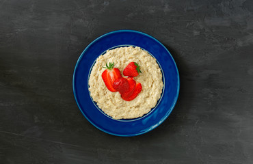 Oatmeal porridge with strawberries in vintage blue plate