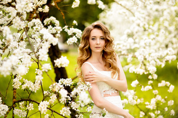 Naklejka premium Spring beautiful girl, blonde, standing in a blooming Apple orchard .