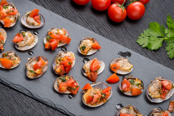 Vongole condite nella loro valva in un piatto di ardesia su un tavolo di legno nero