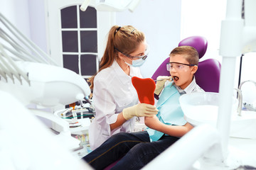 Fototapeta premium dentist shows a denture to the little boy. Boy with smile. very happy boy after the doctor at the clinic, holding a dental jaw in her hands and have a beautiful white smiles. Copy space