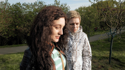 Two smiley merry and cheerful young women or girls friends walking in the green park outdoors in spring against the sunset. Togetherness and friendship positive concept.