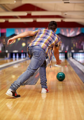 happy young man throwing ball in bowling club