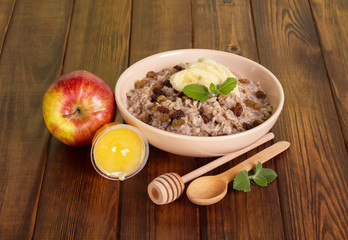 Bowl oatmeal with raisins, honey and apple on  dark tree.