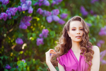 Young beautiful  girl posing near lilac bushes in blossom