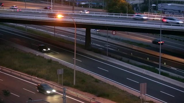 Road traffic scene in the dusk, with bridge in side view, and cars moving in different directions and levels, of entry and exit of Barcelona.