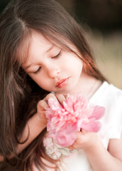 Obraz na płótnie Canvas Cute baby girl 4-5 year old holding pink flower outdoors closeup