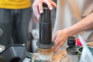 Step by step aero press coffee preparation Bearded barista in blue jeans shirt press aeropress to fill glass with beverage Professional coffee brewing cafe shop

