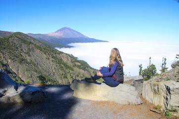 Young  girl with his backpack siting on the rock and contemplating the landscape of volcano Teide...