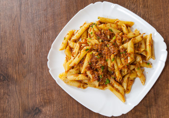 pasta penne with stew meat sauce in a plate on wooden table