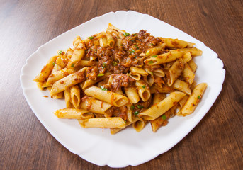pasta penne with stew meat sauce in a plate on wooden table