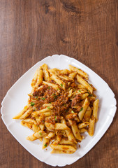 pasta penne with stew meat sauce in a plate on wooden table