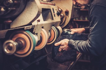 Shoemaker performs shoes in the studio craft grinder machine.
