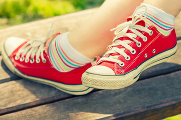 Naklejka premium Woman's feet in a bright red canvas sneakers sitting on a bench.