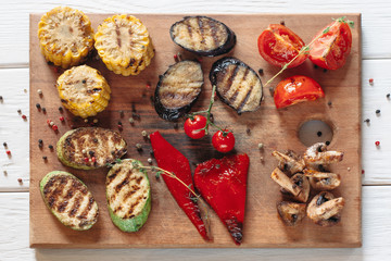 Grilled vegetables on cutting board on white wooden background. Flat lay on vegetable bbq serving. Top view on vegetarian grill set