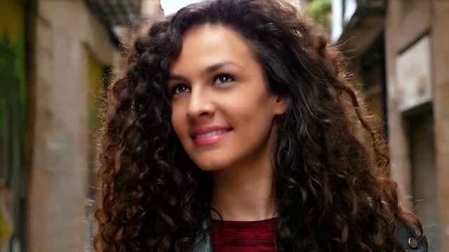 Portrait of happy young woman with beautiful curly hair walking in the city, slow motion