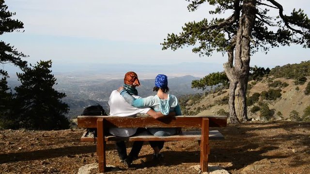 Couple during a trip, rest, sitting on a bench, in front of the beautiful scenery in the mountains. Sunny day in Cyprus. Back view
