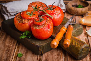 Baked stuffed chicken tomatoes served on cutting board  on wooden background. Selective focus