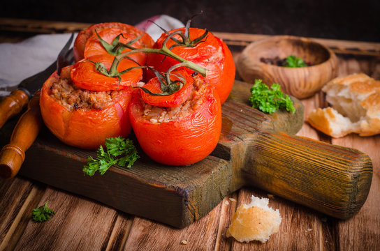 Baked stuffed chicken tomatoes served on cutting board  on wooden background. Selective focus