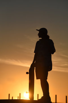Teen boy silhouette with skateboard on summer day