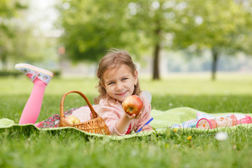 Little girl holding an apple in his hand on a picnic