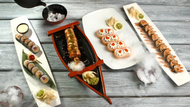 Different plates with sushi rolls. Hand with kettle pouring liquid. Sushi served with dry ice. Artwork created by japanese chef.