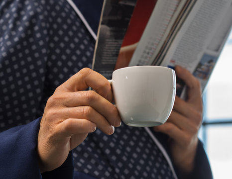 A man in a fashionable bathrobe drinking coffee and reading a magazine