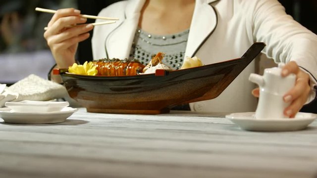 Woman with chopsticks eating sushi. Man's hands with sushi boat. Lunch at japanese cafe. Special dish for regular customer.