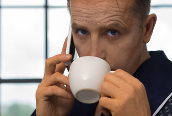 A man in a bathrobe, drinking coffee in the morning and calling on the phone