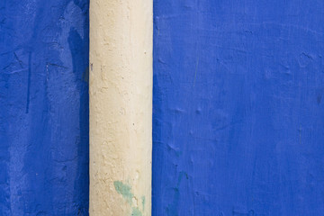 Detail of a rough blue wall with a cream colored pipe.
