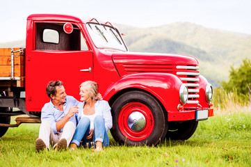 Senior couple sitting at the red vintage car
