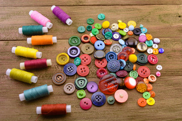 macro handful of multicolored buttons for clothes near multicolored threads on reels for sewing. wooden background