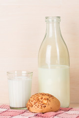 Old fashioned opened bottle of milk stands with faceted glass of milk and a bun on a red squared kitchen towel.