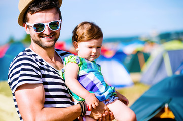 Young father with his baby daughter between tents, summer