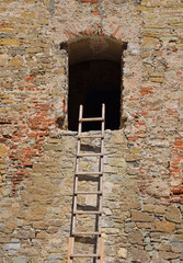 Wooden ladder near window of old stone wall