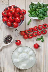 .Mozzarella cheese , cherry tomatoes , basil and pepper lie on a light wooden table .