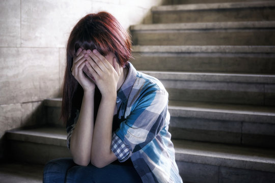 Depressed girl - Girl in adolescent crisis sitting on the steps of a basement, covers her face with her hand.