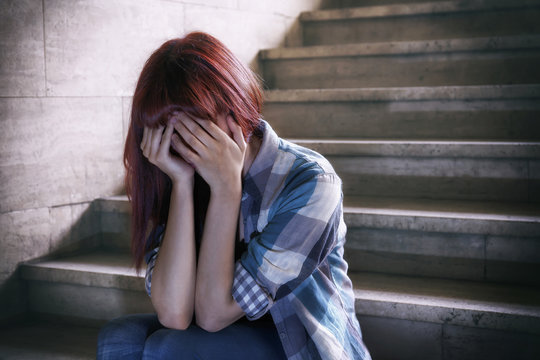 Depressed girl - Girl in adolescent crisis sitting on the steps of a basement, covers her face with her hands.
