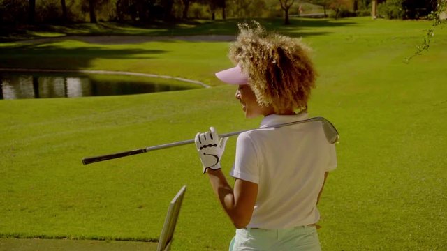 Female golfer standing with her back to the camera and a golf club slung over her shoulder looking to the side waiting for her opponent on the golf course.