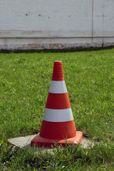 traffic cone with red and white stripes is on the green lawn