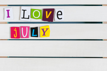 I Love July written with color magazine letter clippings on wooden board. Summer vacation concept, empty space for text