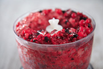 Close focus on blended together in pot frozen berries mix and crashed ice cubes. Half way of preparation tasty healthy smoothie process