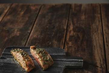 Slightly unfocused two raw pieces of salmon in white wine sause with spices and herbs presented on stone deck prepared for grill Healthy nutrition meal isolated on side of rustic wooden table