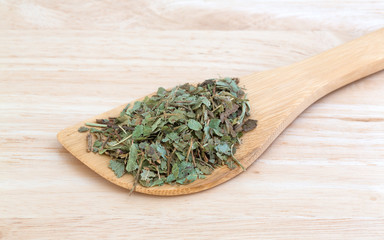 Portion of dried bilberry leaf on a wood spoon atop a wood counter top