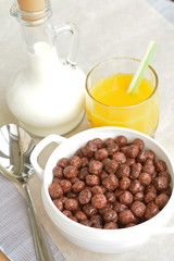 Spoon, bowl with chocolate cereal flakes, milk and juice on the paper